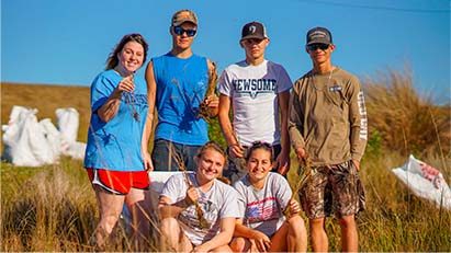 Group of 6 young, smiling volunteers standing in a grassland area.