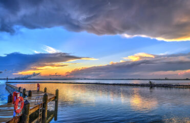 Sunset water scene showing a wooden dock and clouds